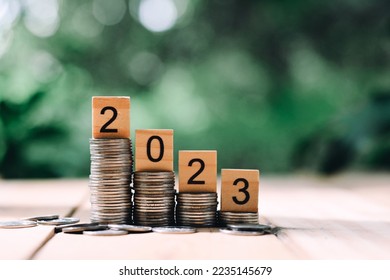 close up stack of coin and 2023 wooden text block on wood table, saving and manage money for new year, e-commerce and shopping online technology, economic crisis risk and problem concept