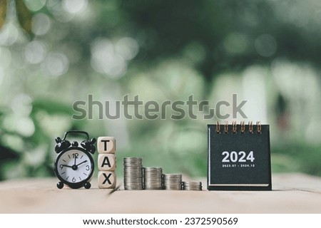 close up stack of coin, 2024 small calendar, wooden tax text and alarm clock on wood table, saving and manage money to success business, planning cash for holiday season concept