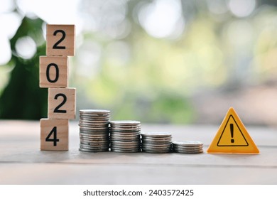 close up stack of coin, 2024 wooden text block and caution sign on wood table, saving and manage money to success business, economic crisis risk and problem concept 