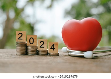 close up stack of coin, 2024 wooden text block, stethoscope and red heart on table, saving and manage money for healthy, medical and healthcare, life insurance business technology concept