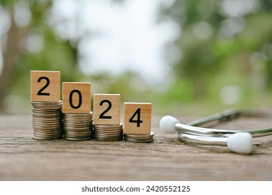 close up stack of coin, 2024 wooden text block and stethoscope on table, saving and manage money for healthy, medical and healthcare, life insurance business technology, economic crisis problem 