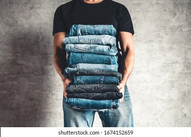 Close Up Stack Of Folded Denim Blue Jeans In Hand Over Gray Wall Background, Copy Space