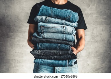 Close Up Stack Of Folded Denim Blue Jeans In Hand Over Gray Wall Background, Copy Space