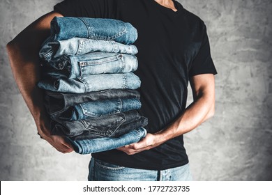 Close Up Stack Of Folded Denim Blue Jeans In Hand Over Gray Wall Background, Copy Space