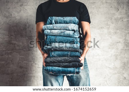 close up stack of folded denim blue jeans in hand over gray wall background, copy space
