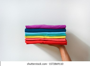 close up stack folded multicolored t  shirt in hand over white background  copy space