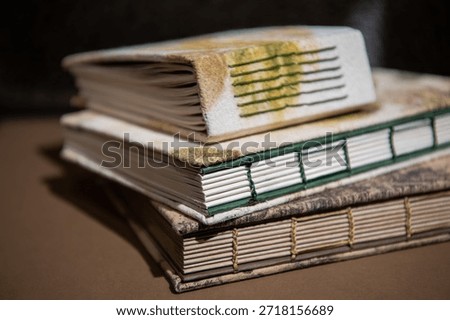 Close up of a stack of handcrafted eco-print notebooks with floral and leaf-patterned covers. Artistic hand-sewn binding and organic textures in a dark studio setting.
