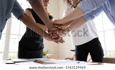 Close up stack hands over table of diverse international company workers. Mixed race young colleagues joining hands, showing support before starting new project, involved in teambuilding activity.
