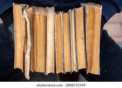 Close up of a stack of old antique and secondhand books with aged yellowed pages and worn multi colored covers, representing a texture, background, literature, and history.