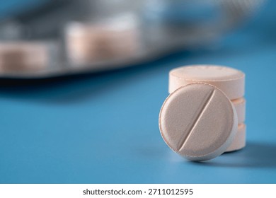A close up of stack of pills on a blue surface. The pills are pink.