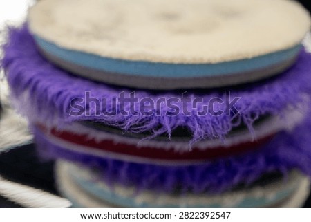 Close up of a stack of professional car detailing buffing pads. Multicolored wool and microfiber polishing wheels for electric dual action orbital machines in a garage auto workshop service station shop to restore paint gloss clearcoat surface.