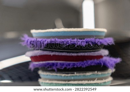 Close up of a stack of professional car detailing buffing pads. Multicolored wool and microfiber polishing wheels for electric dual action orbital machines in a garage auto workshop service station shop to restore paint gloss clearcoat surface.