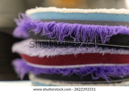Close up of a stack of professional car detailing buffing pads. Multicolored wool and microfiber polishing wheels for electric dual action orbital machines in a garage auto workshop service station shop to restore paint gloss clearcoat surface.
