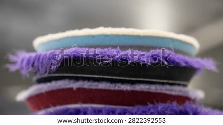 Close up of a stack of professional car detailing buffing pads. Multicolored wool and microfiber polishing wheels for electric dual action orbital machines in a garage auto workshop service station shop to restore paint gloss clearcoat surface.
