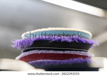 Close up of a stack of professional car detailing buffing pads. Multicolored wool and microfiber polishing wheels for electric dual action orbital machines in a garage auto workshop service station shop to restore paint gloss clearcoat surface.