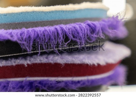 Close up of a stack of professional car detailing buffing pads. Multicolored wool and microfiber polishing wheels for electric dual action orbital machines in a garage auto workshop service station shop to restore paint gloss clearcoat surface.