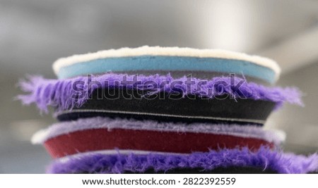 Close up of a stack of professional car detailing buffing pads. Multicolored wool and microfiber polishing wheels for electric dual action orbital machines in a garage auto workshop service station shop to restore paint gloss clearcoat surface.