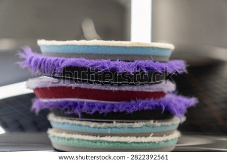 Close up of a stack of professional car detailing buffing pads. Multicolored wool and microfiber polishing wheels for electric dual action orbital machines in a garage auto workshop service station shop to restore paint gloss clearcoat surface.