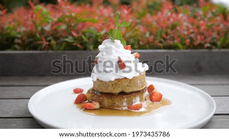 Close up of a stack of vegan pancakes decorated with plant based whipped cream and strawberries. Healthy breakfast concept