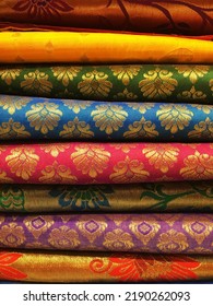 Close Up Of Stacked Fabric In The Indian Fabric Shop. Exquisite Indian Textile With Golden Patterns. 