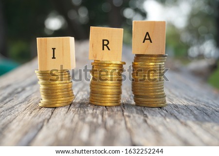 Close up of stacking gold coins and wooden blocks written IRA on nature background and natural lighting. Individual Retirement Accout concept 