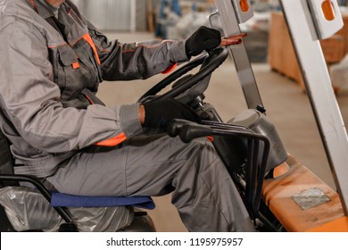 Close - Up Steering Wheel And Levers. Man Driving A Forklift Through A Warehouse In A Factory. Driver In Uniform And Protective Helmet. The Concept Of Logistics And Storage