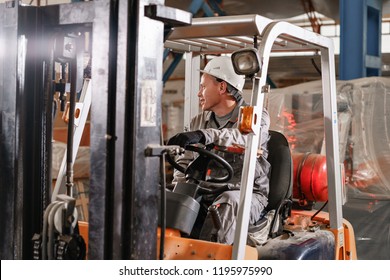 Close - Up Steering Wheel And Levers. Man Driving A Forklift Through A Warehouse In A Factory. Driver In Uniform And Protective Helmet. The Concept Of Logistics And Storage