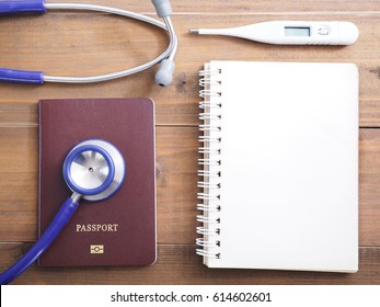 Close up stethoscope, passport, thermometer and blank notepad on wood background, top view