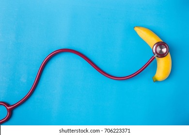 Close up Stethoscope and yellow banana on blue background. For men penis check up concept. With empty free space for text or design. Top view.