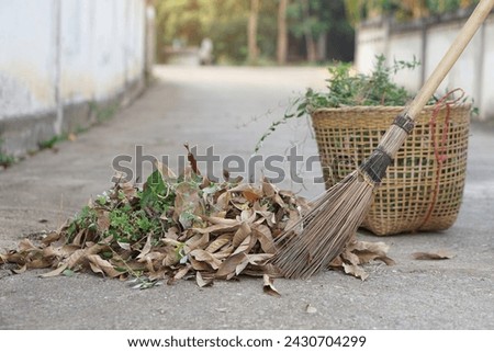 Close up stick broom sweeps dry leaves and weeds, keep into basket to for throw away garbage. Concept, cleaning street in community area. Get rid of grass and garbage beside street.                   