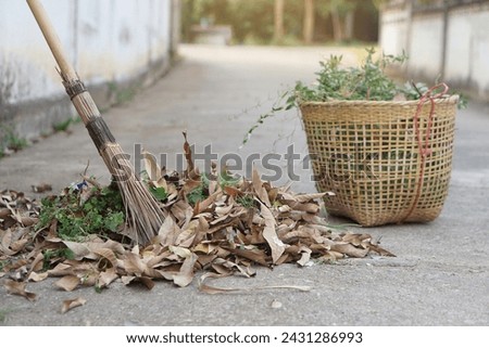 Close up stick broom sweeps dry leaves and weeds, keep into basket to for throw away garbage. Concept, cleaning street in community area. Get rid of grass and garbage beside street.                   