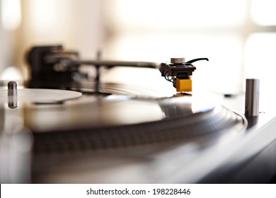 Close Up Still Life Detail View Of A Record Player Playing Music With The Needle Touching The Groove Of The Album Against A Sunny Golden Window In A Music Club Interior. DJ Equipment Working In Venue.