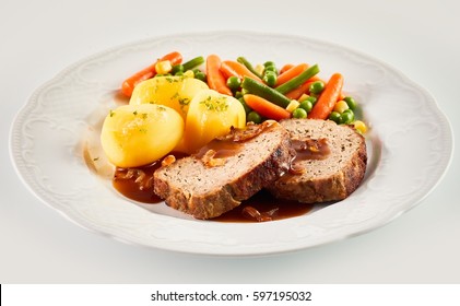 Close Up Still Life Of Hearty Dinner Meal - Slices Of Meatloaf With Brown Gravy, Roasted Potatoes, And Mixed Vegetables Served In White Dish On White Background