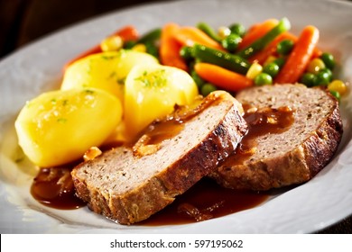 Close Up Still Life Of Hearty Dinner Meal - Slices Of Meatloaf With Brown Gravy, Roasted Potatoes, And Mixed Vegetables Served In White Dish On White Background