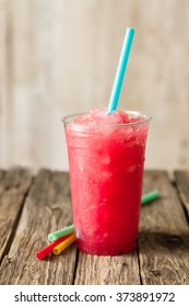 Close Up Still Life Profile View Of Refreshing Frozen Red Slush Drink Served On Rustic Wooden Table With Colorful Drinking Straws