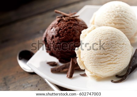 Close Up Still Life of Scoops of Chocolate and Vanilla Ice Cream with Chocolate Shavings and Vanilla Beans on Modern White Plate with Spoon on Rustic Wooden Table Surface with Copy Space