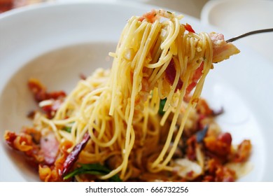 Close up stir fried spaghetti with mushroom, bacon, garlic , cheese and dried chilli with fork - Shutterstock ID 666732256