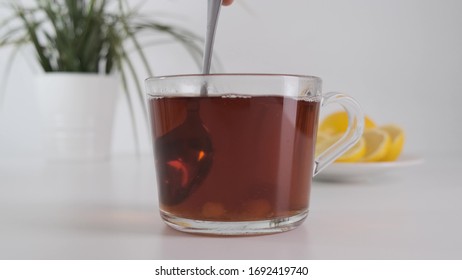 Close up stirring sugar with metal spoon in transparent glass cup tea on white table. Slow motion.