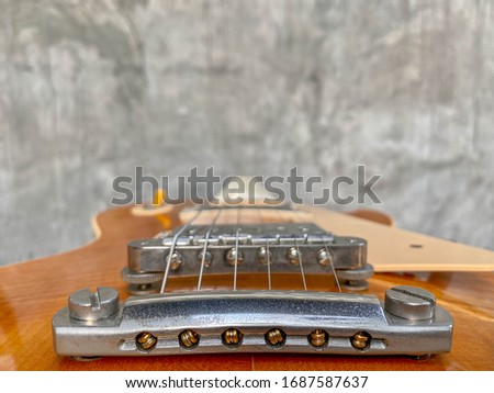 Close up stop tail bridge and the ball end stings of honey burst electric guitars with blurred grey concrete grunge style. wallpaper or background with copy space for text. music store business. 
