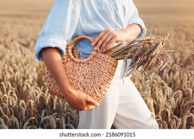 Close Up Of Straw Handbag Filled With Wheat. Woman Holding Summer Purse With Bundle Of Wheat In Field At Sunset