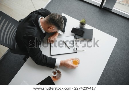 Close up of stressed businessman holding a glass of whiskey he sleeping and Data Charts,business document at office desk. alcohol addiction and drunk businessman concept.