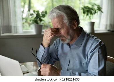 Close up stressed mature man massaging nose bridge, holding glasses, sitting at desk with laptop, elderly grey haired male suffering from eye strain, dry eyes syndrome after long laptop use - Powered by Shutterstock