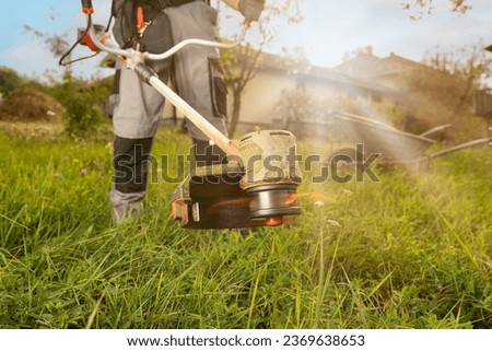 Close up of string grass cutting trimmer held by worker in protective clothing. Gardening concept.