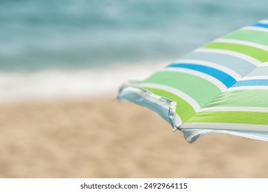 close up of a striped beach umbrella with sea and sand in the background copy space - Powered by Shutterstock