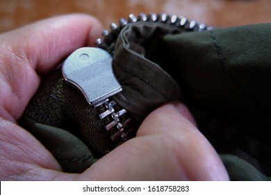 A close up of stuck zipper on a dark green jacket, holding by a hand
