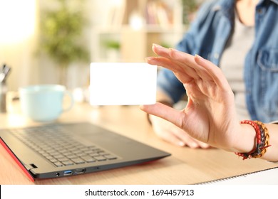 Close up of student girl hand showing blank credit card to camera sitting on a desk at home