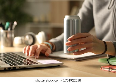 Close up of student girl hands holding energy drink can at night studying on a desk at home