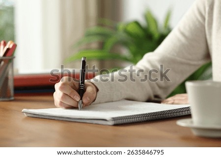 Close up of student hand taking notes on notebook on wooden table at home