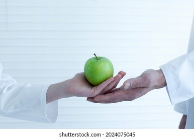 Close Up Of Student Hand Wears Lab Coat Giving Green Apple To Science Teacher In Lab, Selective Focus