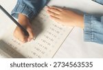 Close up student hands solves mathematics examples. The child holds the pencil in his hand. Notebook sheet with addition table examples. Kids education Concept.